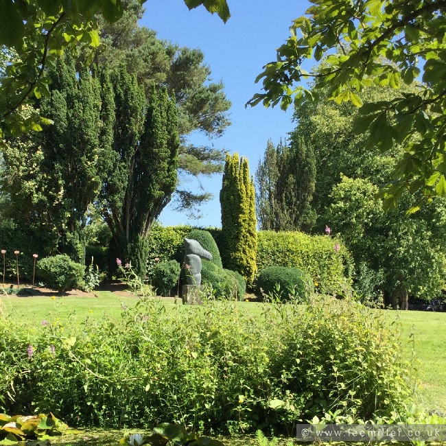 Magic Stallion sculpture stands in Farley['s garden on a sunny day, surrounded by green trees and blue sky